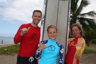 Three people posing with a surfboard on a tropical beach